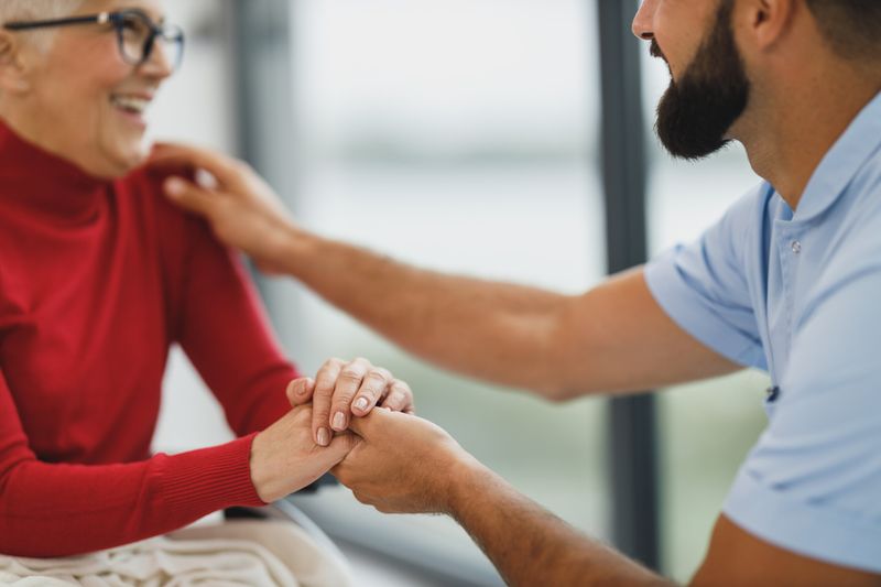 Un cuidador apoya la mano en el hombro de una señora mayor